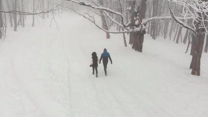 追踪后景情侣牵手一起走在被白雪皑皑神秘宁静景观包围的冬季森林里。佐治亚州精彩的萨巴杜里森林