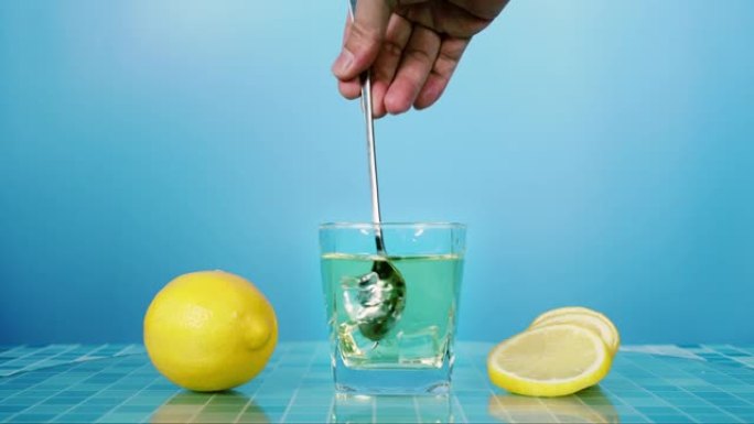 在蓝色背景的桌子上的玻璃杯中搅拌新鲜的柠檬汁