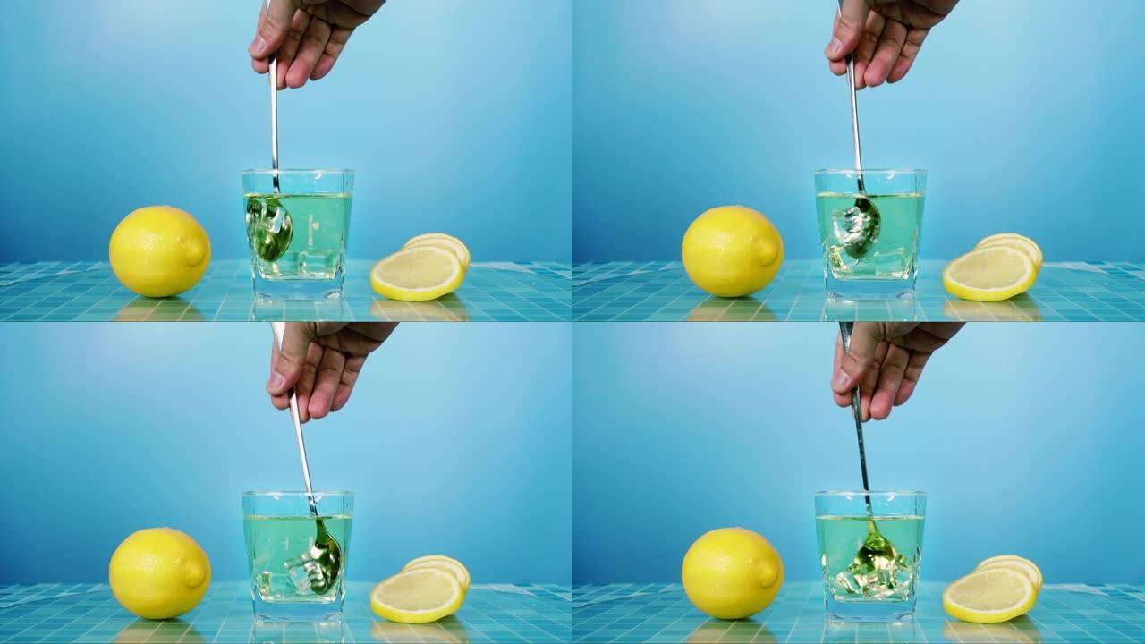 在蓝色背景的桌子上的玻璃杯中搅拌新鲜的柠檬汁