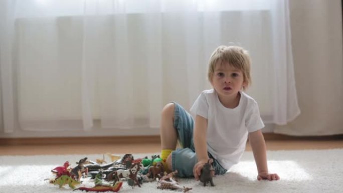 金发孩子，蹒跚学步的男孩，在家玩塑料动物玩具