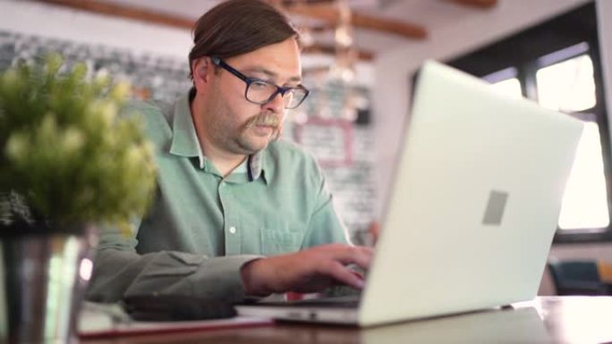 中年专注的男性记者，在自助餐厅工作时在笔记本电脑上键入新文章