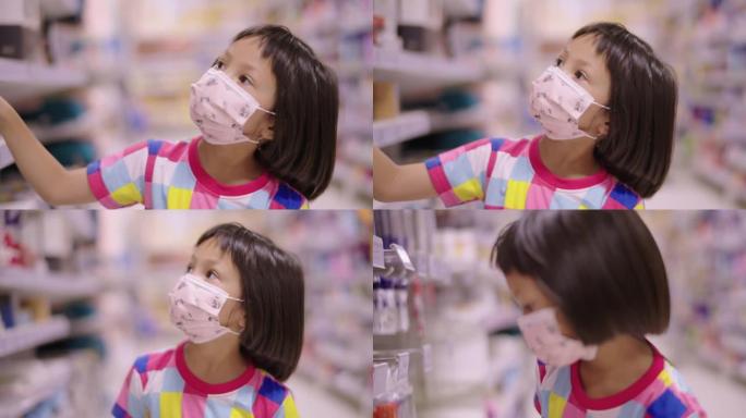 戴着口罩的亚洲女童在当地一家超市散步，看着货架上的产品。