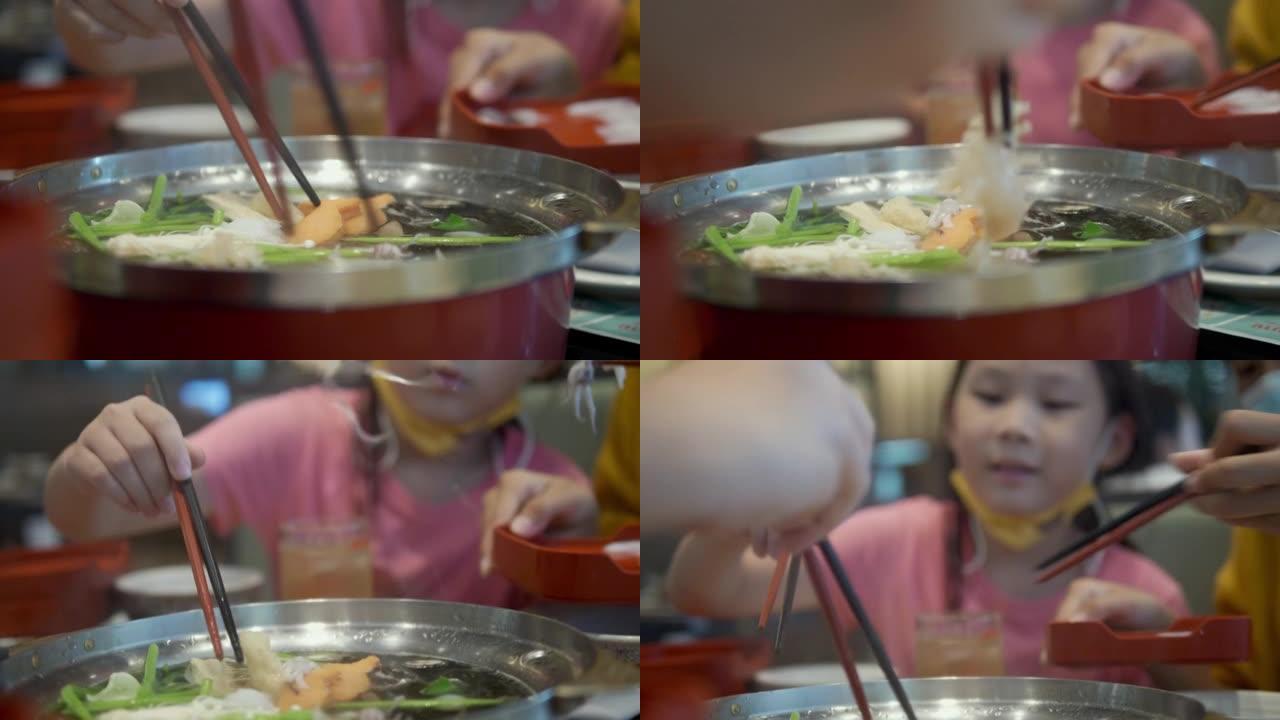 亚洲儿童在餐厅里吃sha锅 (Sukiyaki) 或火锅日本料理，并与家庭，生活方式相结合。