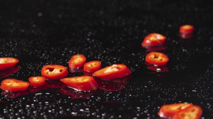 红辣椒片落在潮湿的黑色表面上。麻辣蔬菜，苦菜的成分。餐厅素食壁纸。特写。慢动作