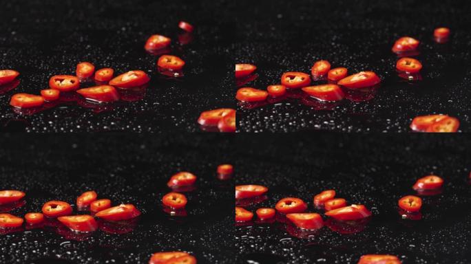 红辣椒片落在潮湿的黑色表面上。麻辣蔬菜，苦菜的成分。餐厅素食壁纸。特写。慢动作