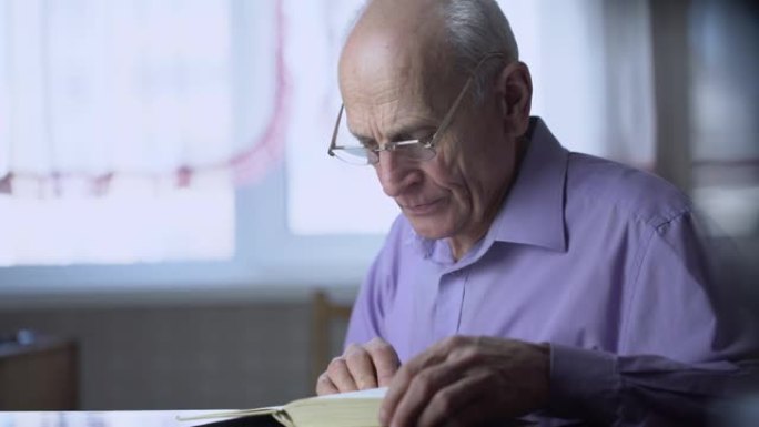 一位戴着眼镜、头发花白的老人坐在桌旁大声读书