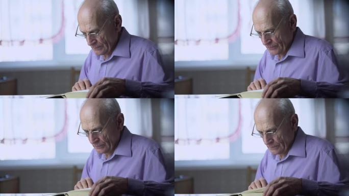一位戴着眼镜、头发花白的老人坐在桌旁大声读书