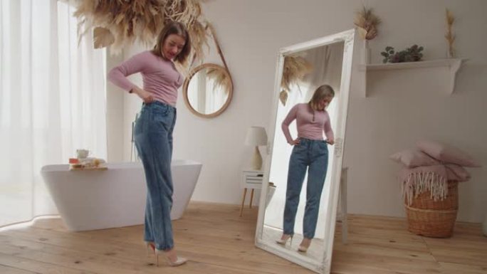 漂亮快乐的女性在室内穿旧牛仔裤展示了她的减肥