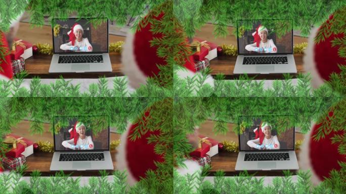 圣诞节期间，戴着圣诞老人帽子的父亲和儿子身上的绿色树枝在笔记本电脑上放着录像带