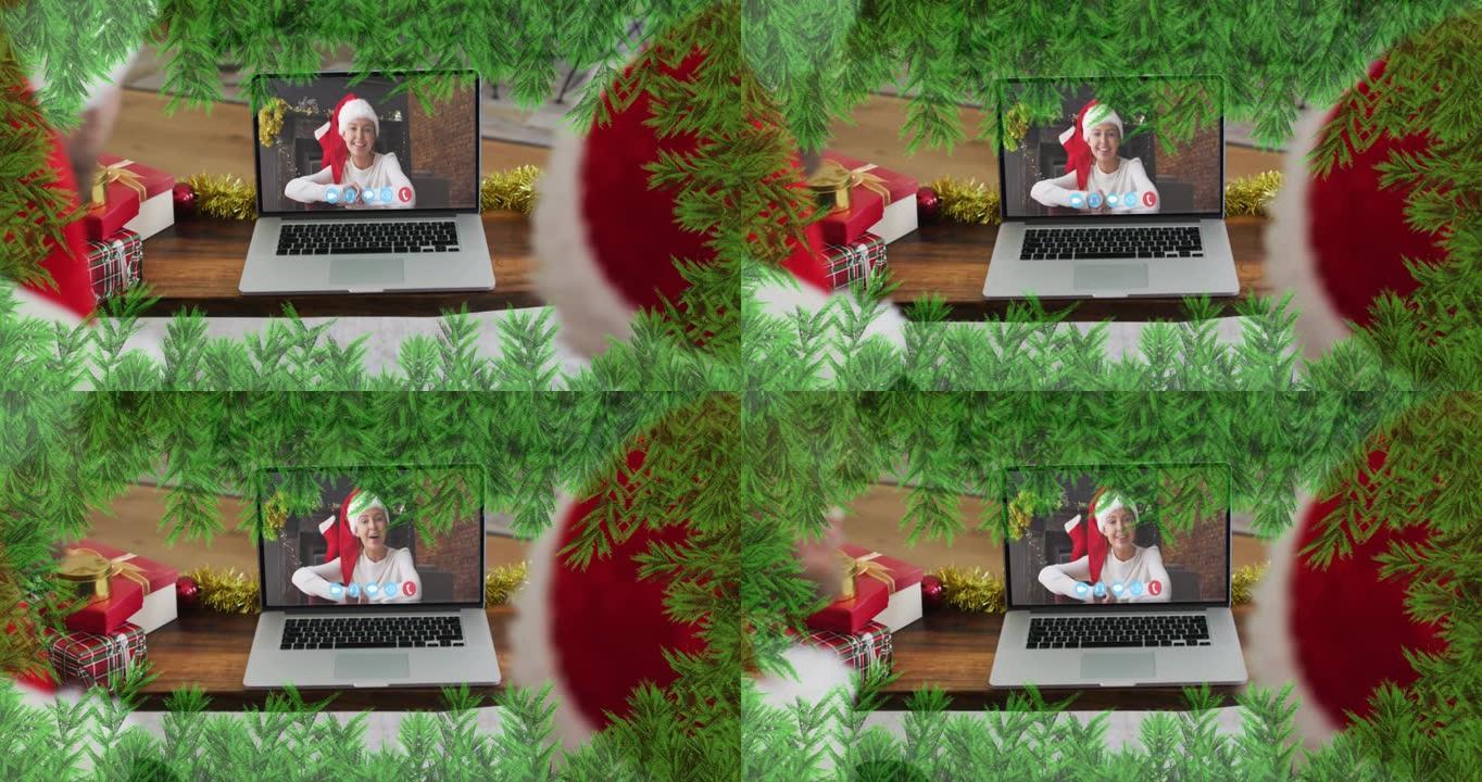圣诞节期间，戴着圣诞老人帽子的父亲和儿子身上的绿色树枝在笔记本电脑上放着录像带