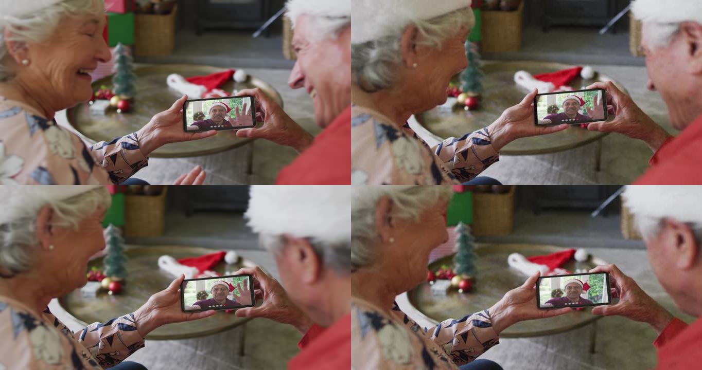 微笑的白人高级夫妇使用智能手机与屏幕上的男人进行圣诞节视频通话
