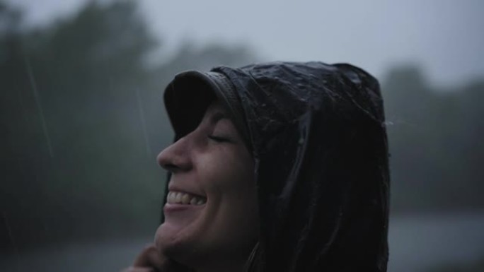 雨中微笑的女人穿着雨衣享受大自然。水滴落在他脸上，女孩很高兴。自然、自由、纯洁的概念...