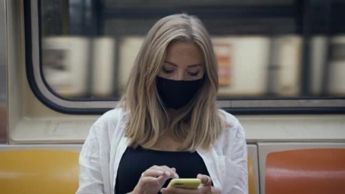 地铁列车上的女人戴口罩的乘客坐地铁玩手机
