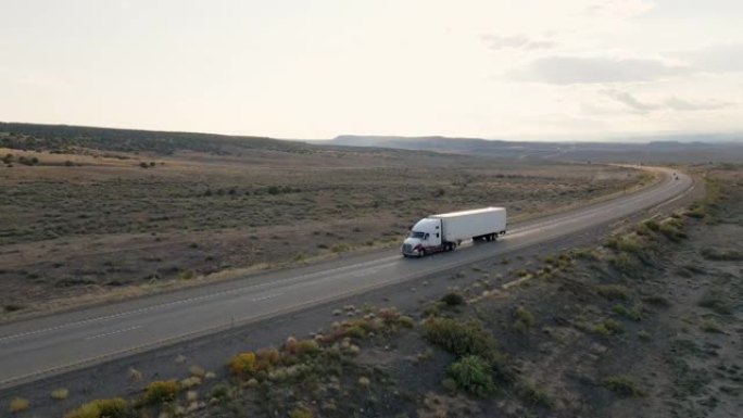 在戏剧性的天空下，半卡车在黄昏时分在犹他州沙漠的高速公路上超速行驶