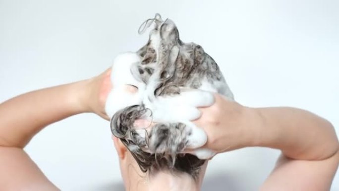 女孩在白色背景上用洗发水洗头，后视图。