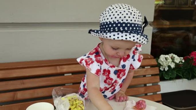 一个穿着彩色连衣裙和圆点帽子的小女孩在城市街头咖啡馆尝试彩色蛋糕