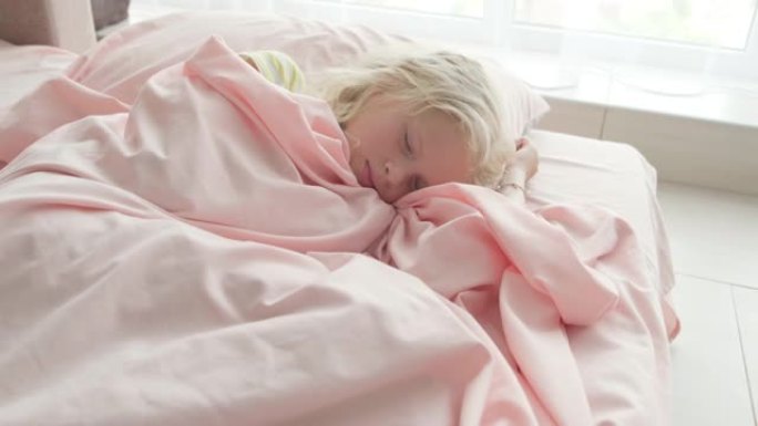 可爱的金发女孩早上在家穿着粉色床单甜蜜睡觉。儿童的梦想，舒适，休息与和平