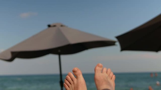 海滩海岸，蓝天。防晒沙滩伞。强风，美丽的屏幕保护程序。和平，文本的空白。男子的腿放在躺椅上