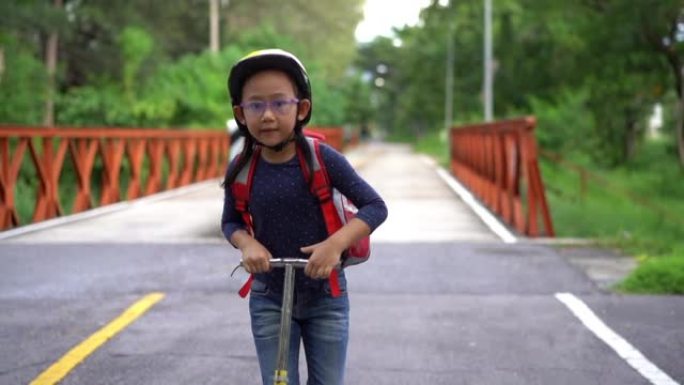 慢动作回到学校。亚洲小女孩背着书包骑着滑板车去上学