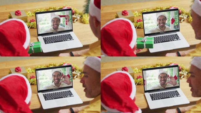 高加索人的父亲和儿子戴着圣诞老人的帽子，使用笔记本电脑进行圣诞节视频通话，屏幕上有男子