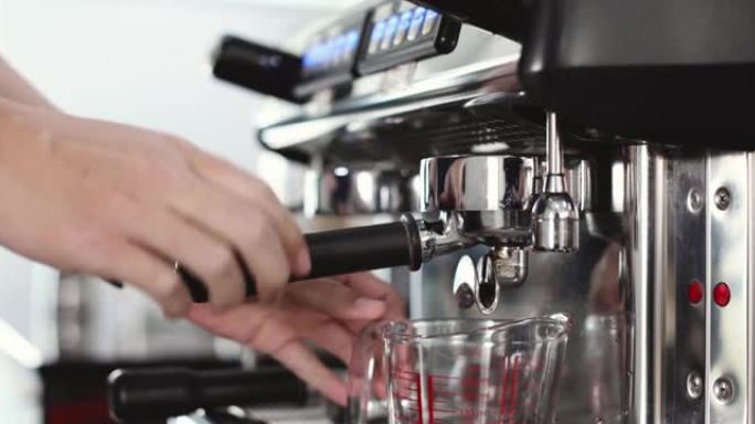咖啡师将装满咖啡粉的portafilter插入机器中，然后按开始按钮，然后将咖啡滴入玻璃杯中，为咖啡