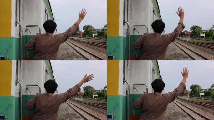 英俊的亚洲年轻人在火车上向朋友打招呼或告别，挥手告别