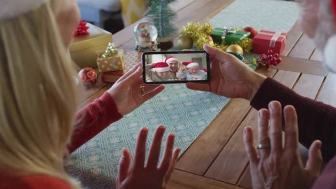 白人夫妇戴着圣诞老人帽子，使用智能手机与家人在屏幕上进行圣诞节视频通话