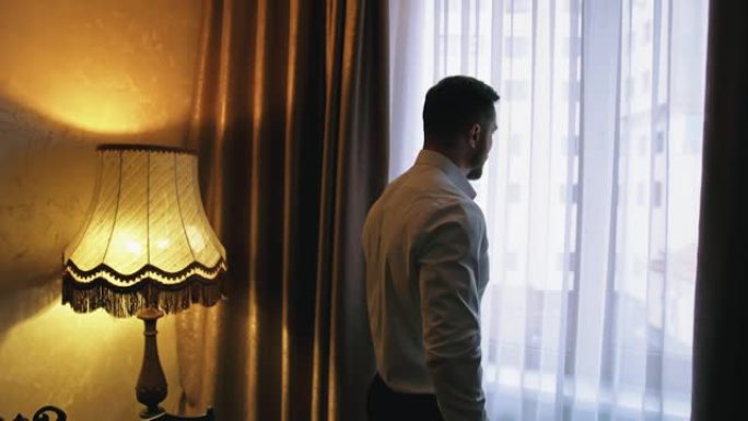 英俊的男人在公寓工作后。黑暗酒店房间窗户附近的年轻商人。男子到达一家酒店。