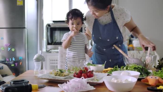 母亲和蹒跚学步的男孩在做蔬菜沙拉。