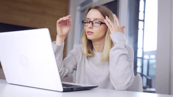 年轻的金发女子戴着眼镜在笔记本电脑上工作，超负荷伸展运动
