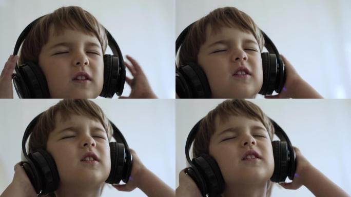 戴着耳机听音乐的可爱的小男孩的肖像。孩子戴着耳机闭着眼睛放松时的慢动作。孩子在家听音乐。快乐无忧无虑