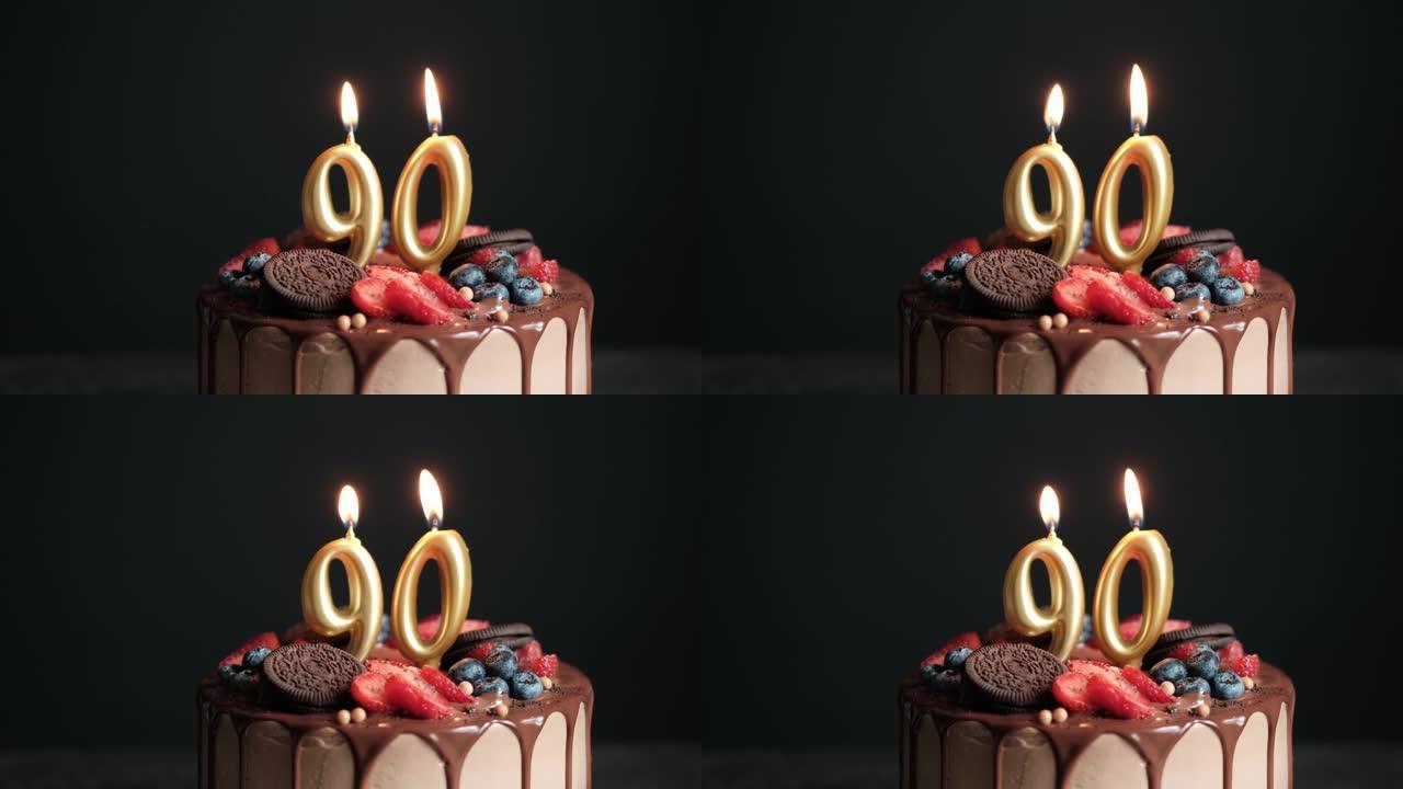 黑色背景上的巧克力生日蛋糕，带有90号金色蜡烛。90周年生日蛋糕。慢动作