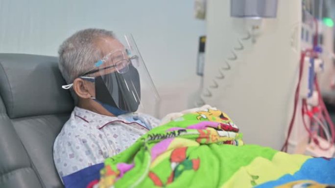 亚洲华人老人坐在椅子上，戴着面罩，正在医院接受透析治疗