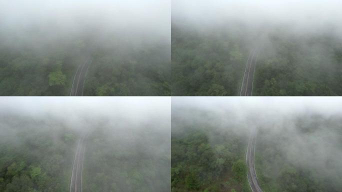 空中无人机电影拍摄的汽车和道路在早上下雨后越过山顶，有雾和绿色森林。