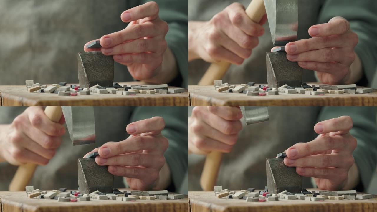 男性的手使用特殊的锤子将马赛克瓷砖分成两半。镶嵌图案石材的制备。在创意车间手工制作。特写。慢动作