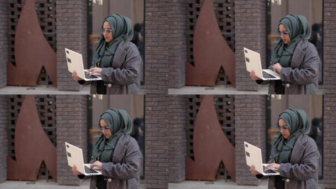 穆斯林妇女使用笔记本电脑站在外面