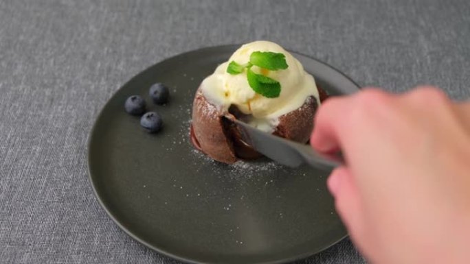 熔岩蛋糕是一种巧克力软糖蛋糕，配以香草冰淇淋，蓝莓，薄荷和咖啡。传统法国糕点。女人割伤