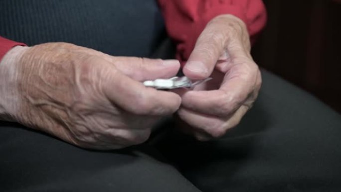 一位老妇人的手拿着一包药片，拆开几颗吃药用的药片