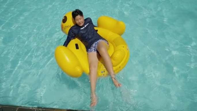 快乐的亚洲男孩在游泳池里的黄鸭橡皮筏上放松，与家人一起度假，生活方式理念。
