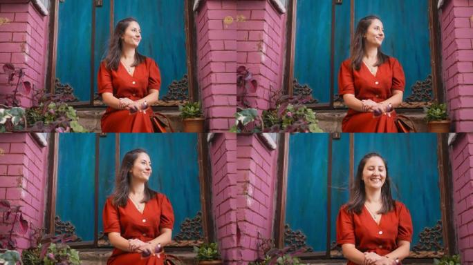 穿着红色长裙的美女坐在台阶上，在城市里对着镜头微笑