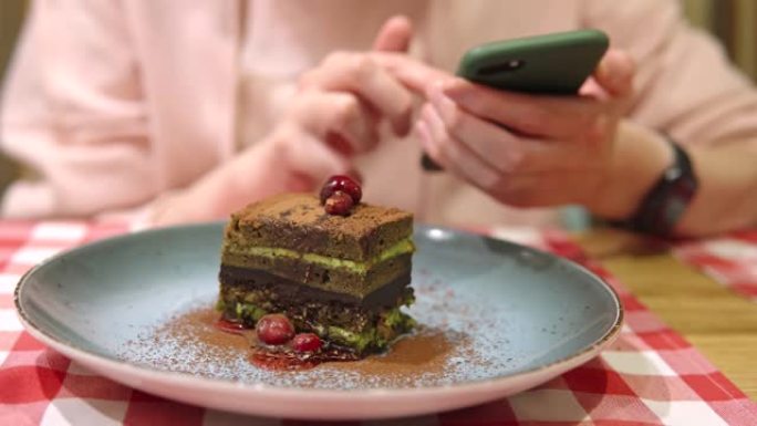 一名妇女使用智能手机，信使，进行在线购物并吃抹茶奶油巧克力蛋糕