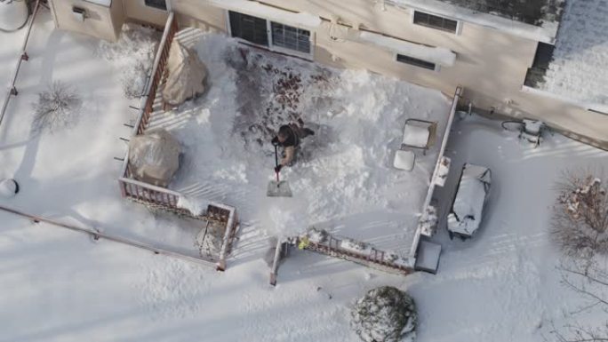 一名成年男子在冬季降雪后用铁锹从雪地上清理门廊。无人机慢动作视频正上方鸟瞰。