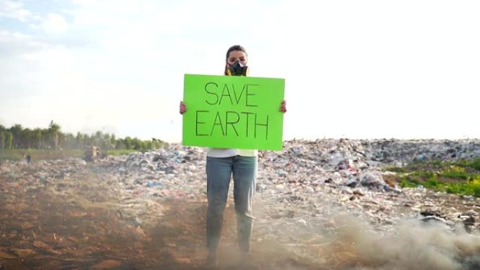 手握海报的年轻女性活动家save earth站在垃圾填埋场中间，戴着呼吸器脸
