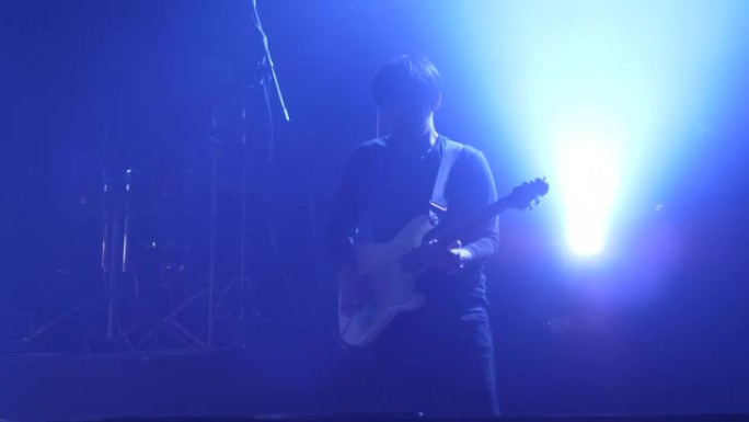 音乐家在舞台上用雾和蓝光演奏电子吉他