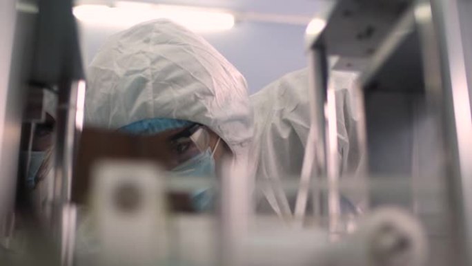 研究医用口罩工厂洁净室，工程师和科学家穿着工作服与数字平板电脑交谈