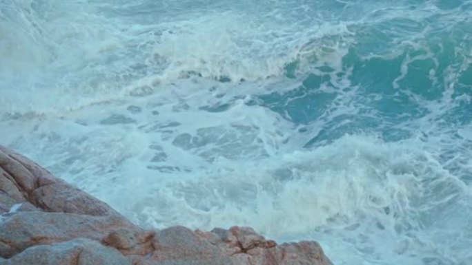 强大的海浪溅到海中的一块大石头上。在岩石热带海岸附近的岩石上冒泡的猛烈破浪