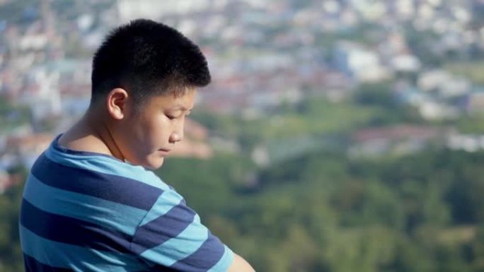 亚洲男孩坐在山顶上，在阳光明媚的日子里看着城市的景色，生活方式的概念。