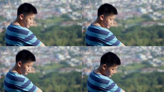 亚洲男孩坐在山顶上，在阳光明媚的日子里看着城市的景色，生活方式的概念。