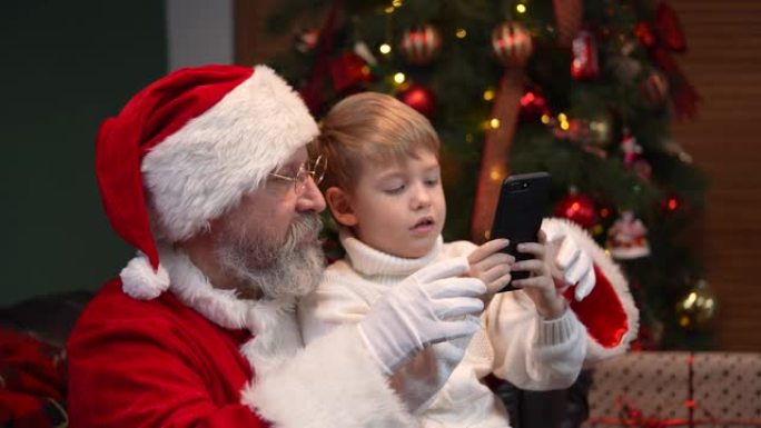 圣诞老人和一个小男孩点击智能手机，在互联网上选择圣诞礼物。电子商务。新年精神、节日和庆祝活动的概念。