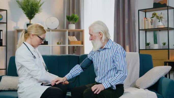 愉快的乐于助人的经验丰富的金发女医生在家探望他时使用眼压计测量老年男性患者的压力